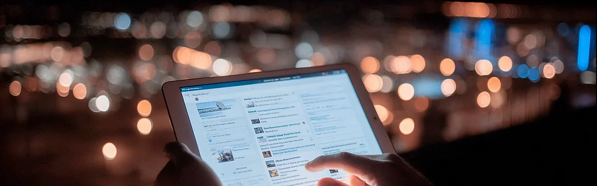 Hände halten ein Tablet mit einem Nachrichten-Feed vor nächtlicher Stadtkulisse – Agenturblog